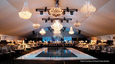 Elegant event tent with crystal chandeliers, dance floor, and stylish black and white decor.