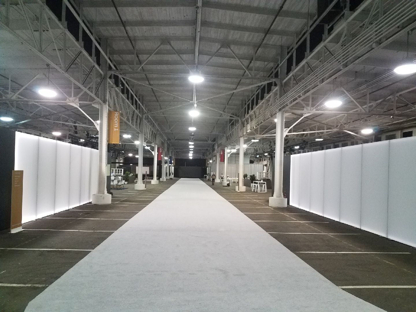 Spacious event venue with white walls, gray carpet, and bright overhead lights for exhibitions.