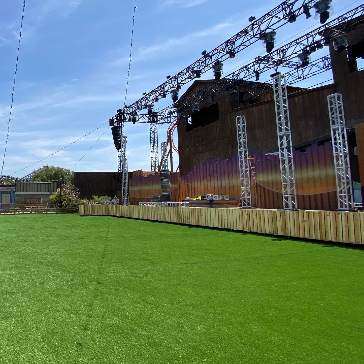 Outdoor concert stage with green artificial grass, colorful backdrop, and stage lighting.