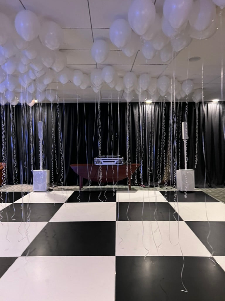 Elegant party decor with white balloons and black curtain backdrop on a checkered floor.