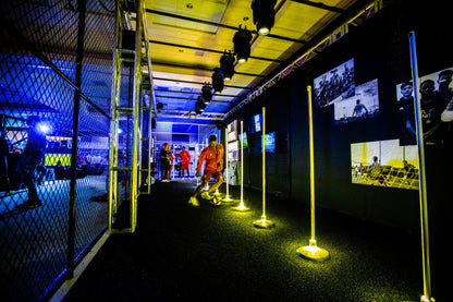 Indoor soccer training area featuring yellow training poles and a player dribbling a ball on synthetic turf.