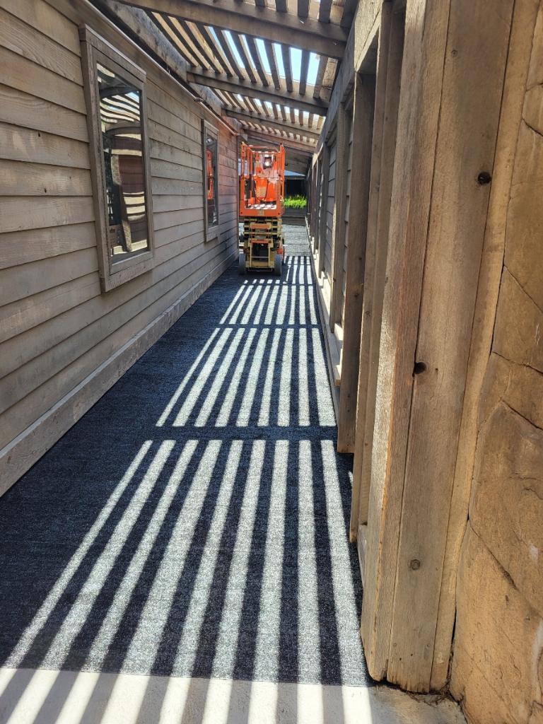 Corrugated walkway with shadows, featuring a sturdy grey carpet and a lift in a wooden structure.