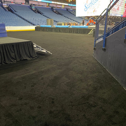 Black carpet flooring in an arena event setup, featuring a stage and seating area.