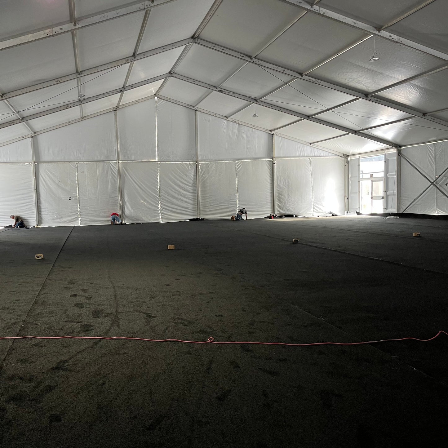 Large white event tent interior with black flooring, workers setting up the space.