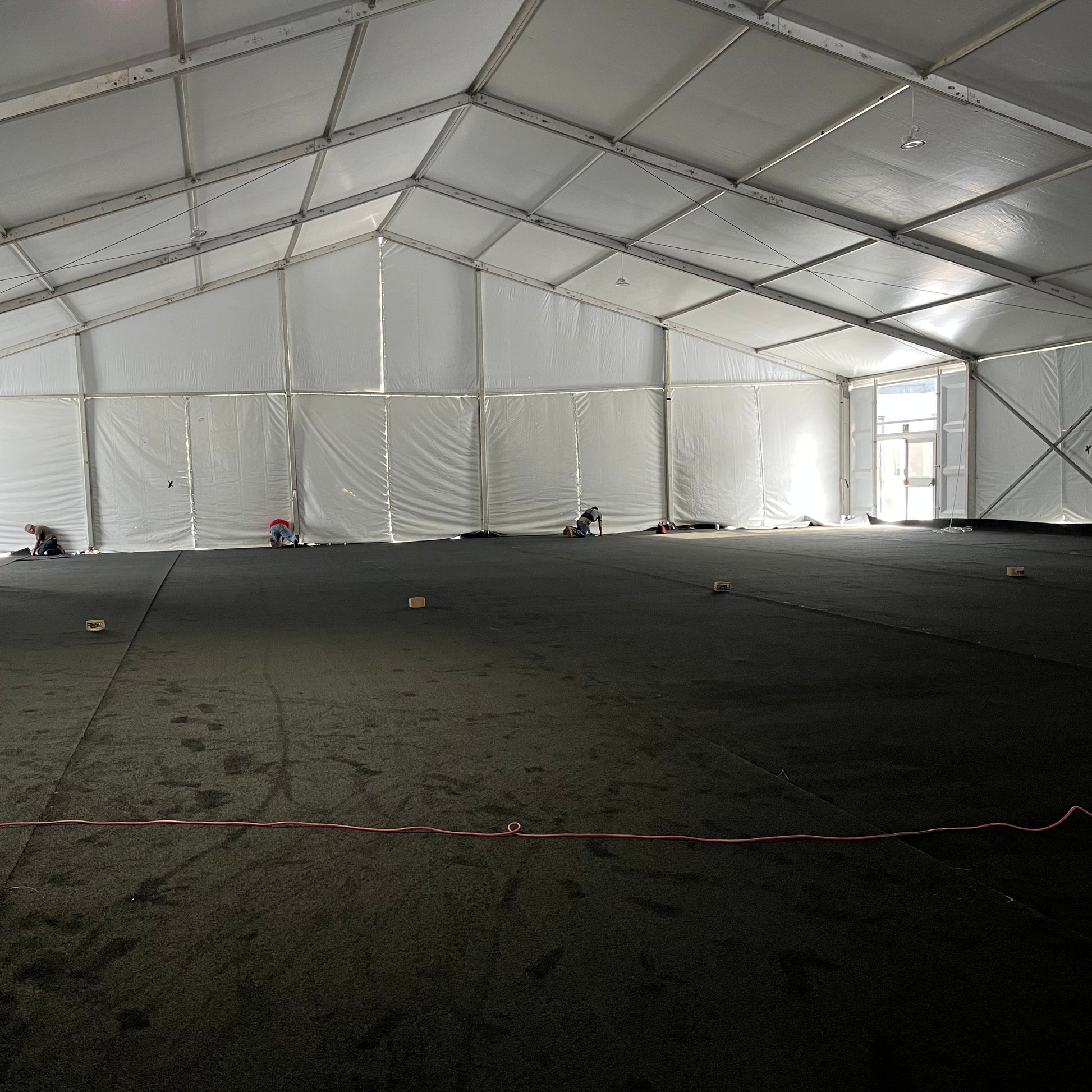 Large white event tent interior with black flooring, workers setting up the space.