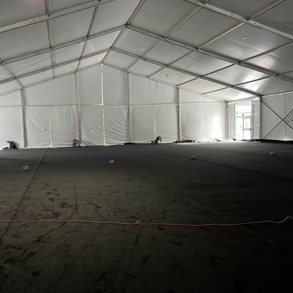 Large white event tent interior with black flooring, workers setting up the space.