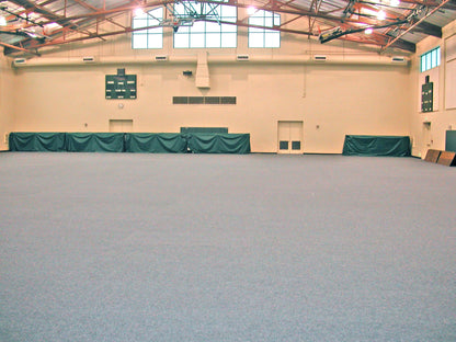 Large indoor sports facility with gray flooring and green protective barriers along the walls.