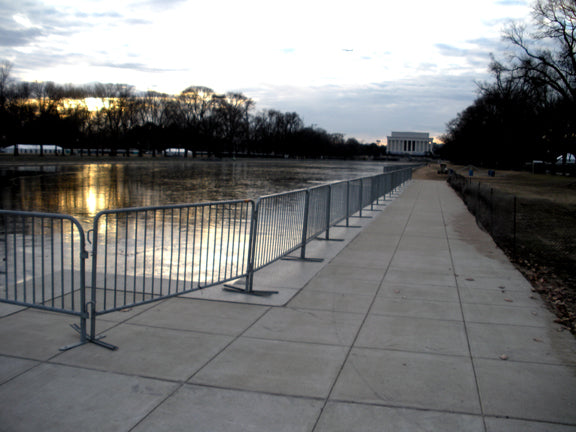 Walkway beside reflective pool with security barriers and trees, leading to the Lincoln Memorial at dusk.