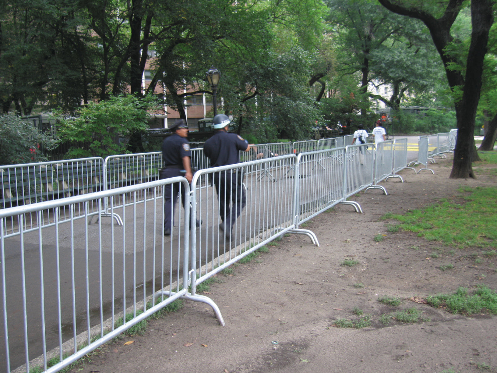 Metal security barriers in a park, used for crowd control, with police officers nearby.