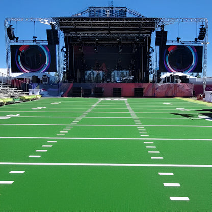 Vibrant green football field stage setup with large screen and sound equipment for events.