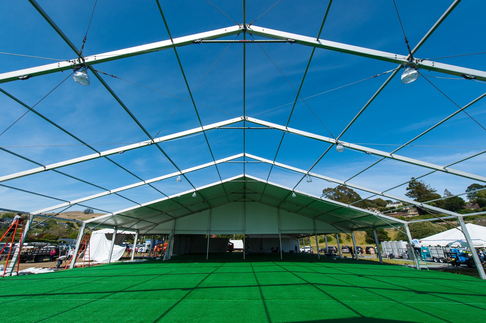 Spacious white event tent interior with green carpet, bright lighting, and clear blue sky.