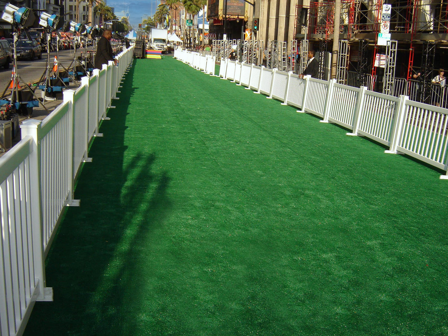 Artificial green carpet walkway with white fencing for events and ceremonies.
