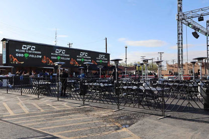 Outdoor event setup with black folding chairs and heating lamps, featuring large sponsor banners.