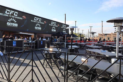 Outdoor event setup with black tables and heaters, featuring sponsor banners in a lively atmosphere.