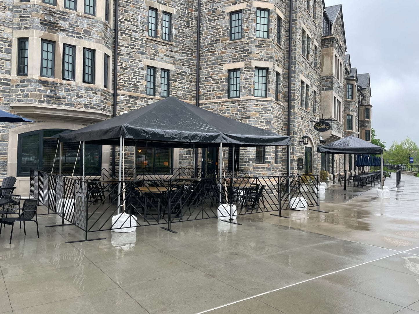 Outdoor dining area with black canopies and chairs, featuring a modern design near a stone building.