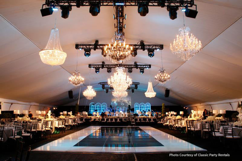 Elegant event tent featuring crystal chandeliers, modern seating, and a polished dance floor.