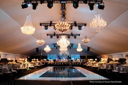 Elegant event tent featuring crystal chandeliers, modern seating, and a polished dance floor.