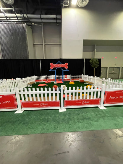 Puppy playground with white fence, colorful toys, and grass flooring, perfect for dogs to play.