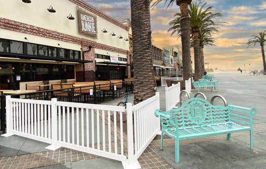 Outdoor beachfront seating area with mint green metal benches and white fencing by a restaurant.