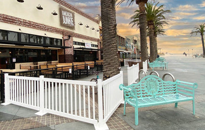Outdoor beachfront seating area with mint green metal benches and white fencing by a restaurant.