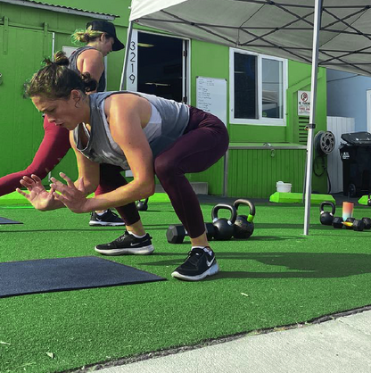 Women exercising outdoors with kettlebells on green turf, wearing athletic wear, focused on training.