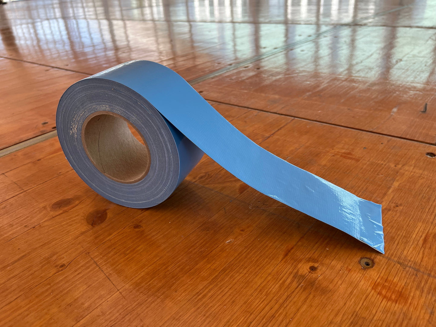 Blue duct tape roll on wooden floor, durable and versatile for repairs and crafting.