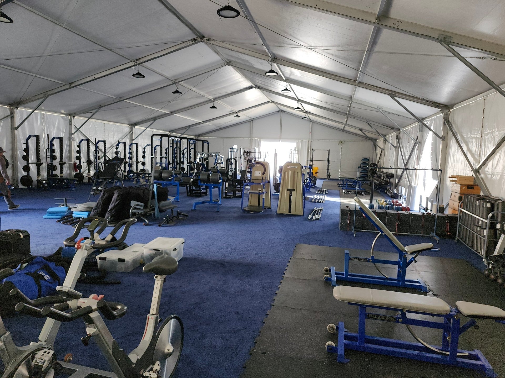 Spacious outdoor gym tent with blue carpet, weight equipment, and exercise bikes for effective workouts.