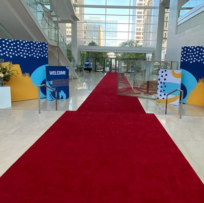 Elegant red carpet entrance with modern colorful welcome signs and glass doors in a bright lobby.