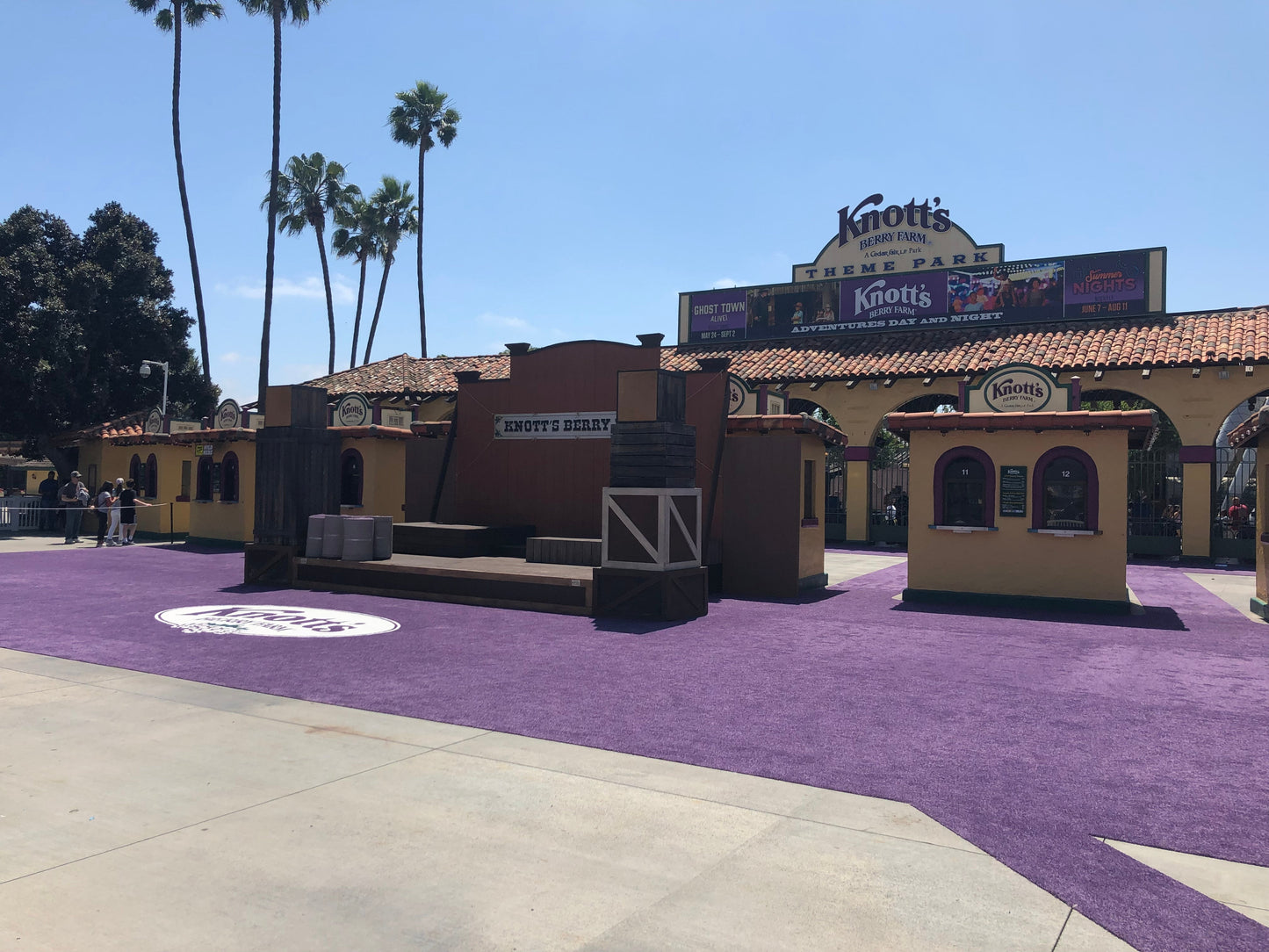 Entrance to Knott's Berry Farm with purple carpet, shops, and sunny palm trees.