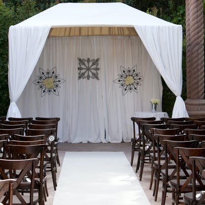 Elegant outdoor wedding altar with white drapes, floral decor, and wooden chairs for guests.