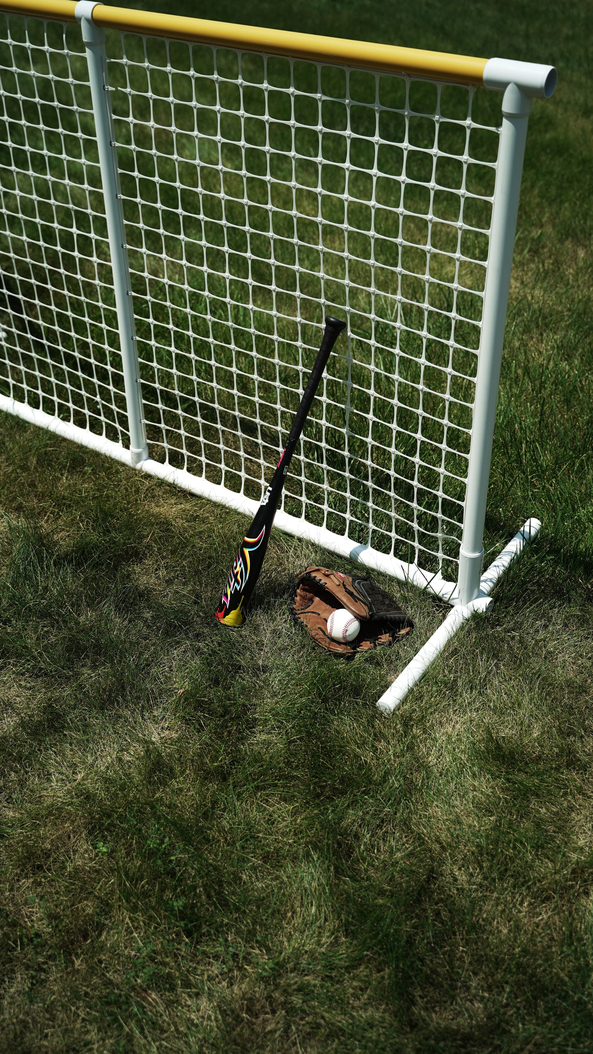 Colorful baseball bat and glove with a ball next to a white net on grassy field.