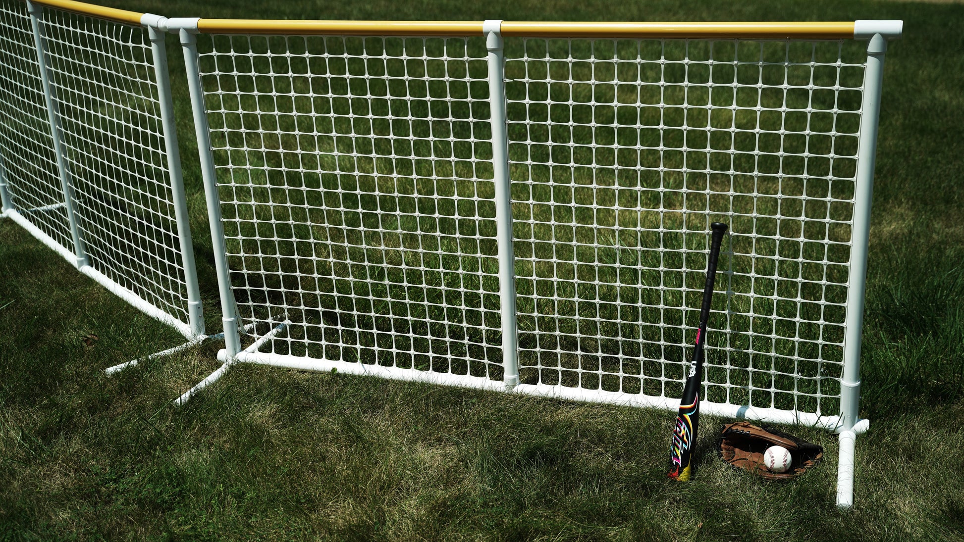 Colorful baseball bat leaning against a white net, with a glove and ball on the grass.