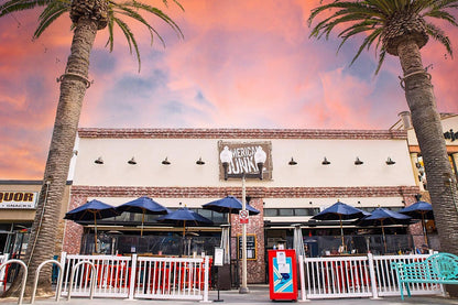 Exterior view of American Junk restaurant with blue umbrellas, red chairs, and palm trees at sunset.