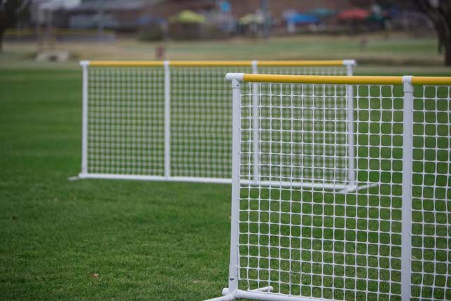 Two durable white soccer goals with yellow top rails on green grass field for sports activities.