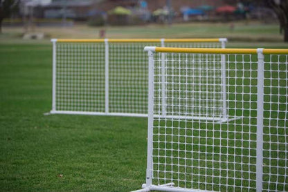 Two durable white soccer goals with yellow top rails on green grass field for sports activities.